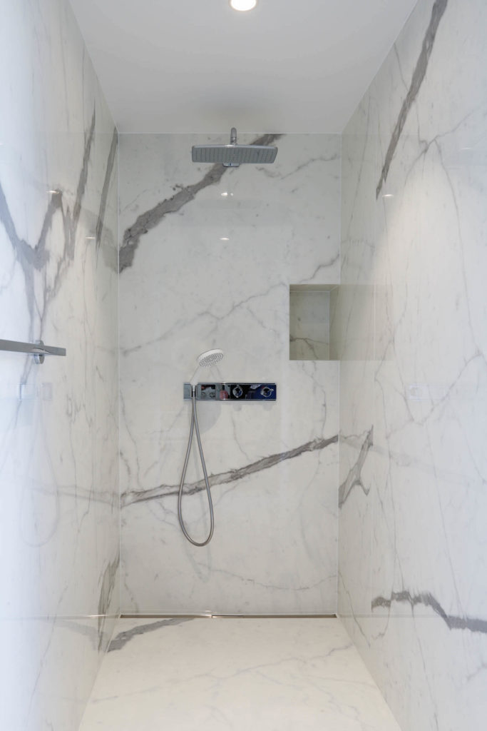 Douche italienne en carrelage grand format imitation marbre blanc avec nervure grise, avec encastre sur la droite.