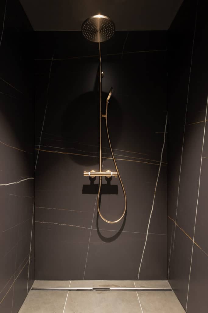 Douche italienne et carrelage grand format dans une maison au bord de l'eau à Rolle. Carrelage imitation marbre et sanitaire doré
