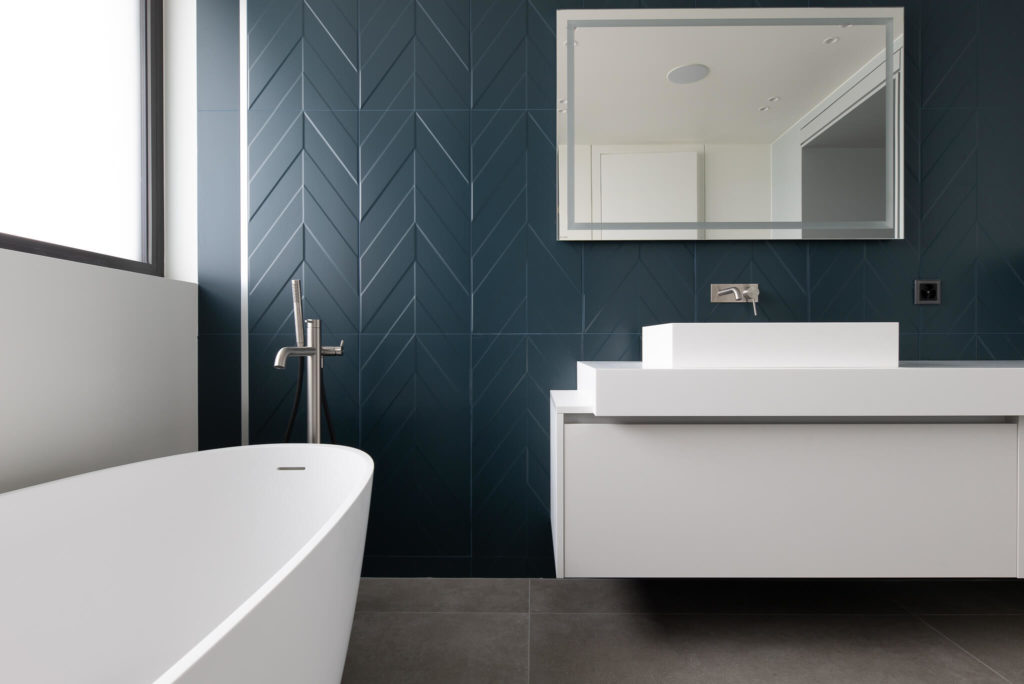 Salle de bain tendance avec carrelage bleu et mobilier design blanc. Maison à Rolle