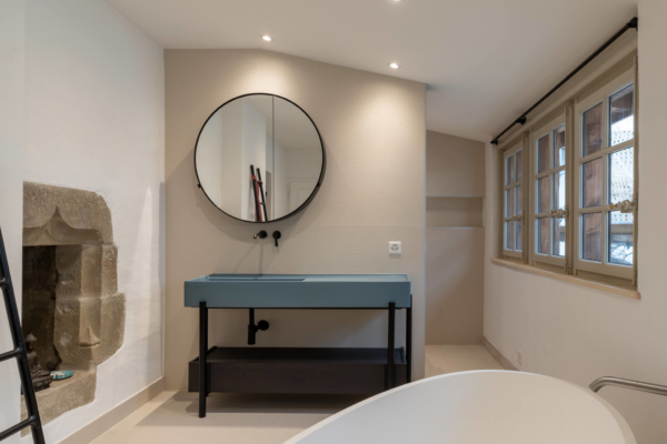 Salle de bains rénovée avec carrelage beige, lavabo et meuble de salle de bain noir et bleu.