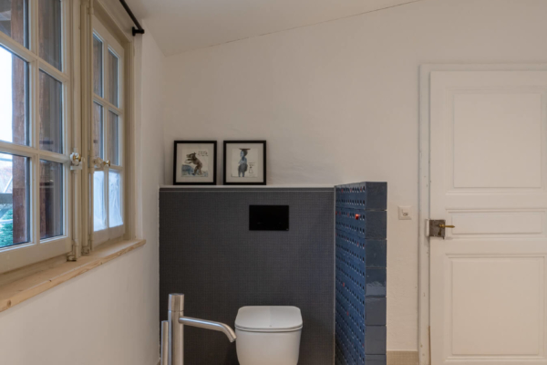 Toilettes dans salle de bains rénovées avec mur en brique bleu pour cacher le wc et baignoire en premier plan