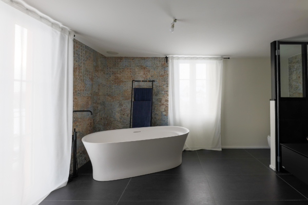 Salle bains avec un sol en carrelage noir et un carrelage à motif, baignoire blanche et lumière naturelle