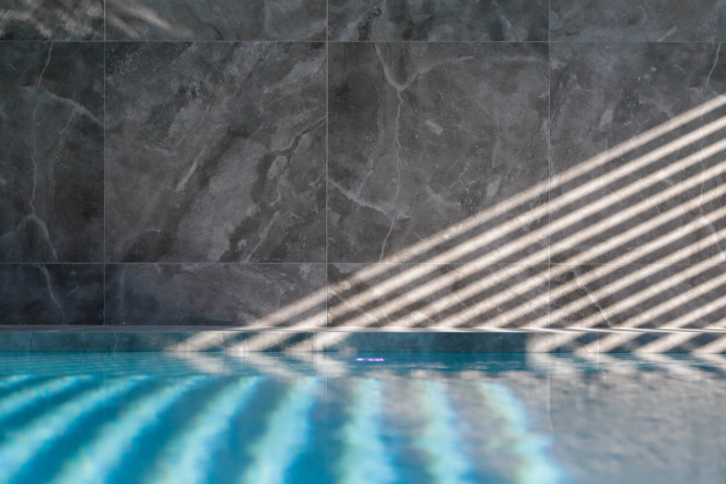 Mur et surface de l'eau d'une piscine intérieur en carrelage imitation pierre