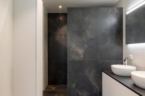 Salle de bains avec carrelage imitation pierre noir au sol, douche italienne avec mur de séparation